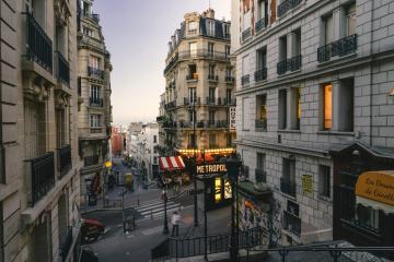 1. A narrow Parisian street at dusk featuring Haussmann-style buildings, a "METROPOL" hotel sign with red-and-white awnings, and a yellow "Le Marais" directional sign on the right.