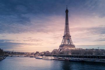 1. The image shows the Eiffel Tower standing prominently beside the Seine River in Paris, with tour boats on the water and a twilight sky.