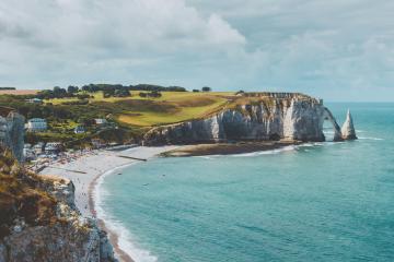 1. A coastal scene featuring a prominent natural limestone arch (the Porte d'Aval) and a smaller stack (the Porte Amont) at Étretat, Normandy, France, with a sandy beach, cliffs, and green fields above.