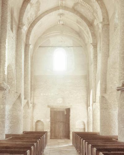 1. The image shows the interior nave of a stone church with massive rounded arches, thick piers, and a barrel-vaulted ceiling, illuminated by bright light from a high window at the far end; wooden pews line the aisle.