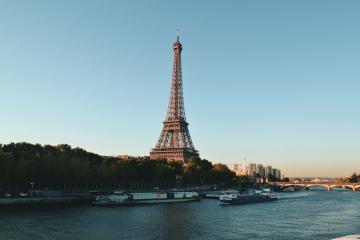 1. The image shows the Eiffel Tower standing prominently beside the Seine River in Paris, with tour boats on the water and a twilight sky.