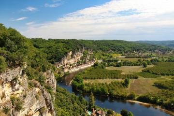 1. A high-angle landscape view of a winding river flowing through a valley with steep limestone cliffs on the left, dense green forests, and a small town nestled along the riverbank under a blue sky with scattered clouds.