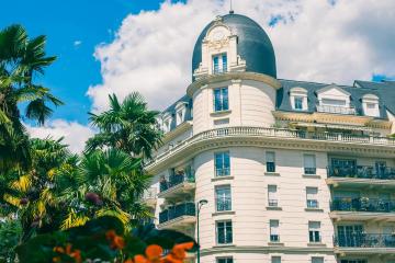 1. A white, multi-story luxury hotel building with a distinctive dark dome and classical architecture, framed by palm trees and orange flowers under a blue sky.