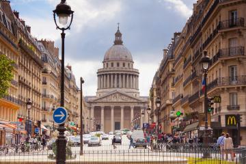 A street scene in Paris, France, looking down Rue de l'Odéon towards the Panthéon, with classic Haussmannian architecture, a McDonald's on the right, and a blue one-way traffic sign on the left.