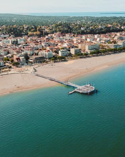 1. An aerial view of a coastal town with a sandy beach, a long wooden pier extending into turquoise water, and a dense urban area backed by forested dunes.
