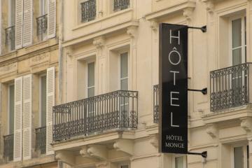 A close-up view of a cream-colored building facade in Paris featuring wrought-iron balconies and a vertical black sign reading "HÔTEL MONGE".