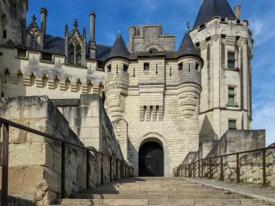 1. A stone Gothic castle with conical-roofed towers, arched gatehouse, and stone staircases leading up to the entrance under a blue sky.