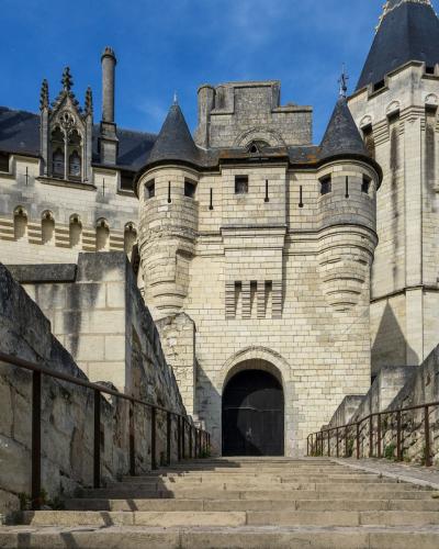 1. A stone Gothic castle with conical-roofed towers, arched gatehouse, and stone staircases leading up to the entrance under a blue sky.