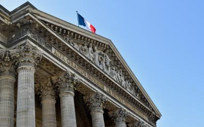 The image shows the pediment and columns of a neoclassical building with a French flag flying atop, and inscribed text on the frieze reading "BANQUE DE FRANCE".