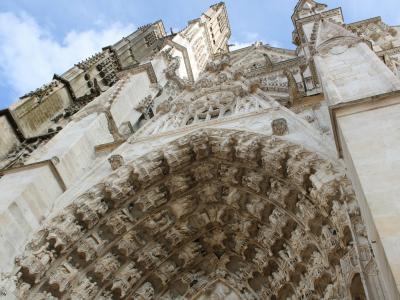 1. A low-angle photograph of the ornate Gothic portal and facade of a large stone cathedral, featuring intricate sculptural details on the tympanum and archivolts under a blue sky.