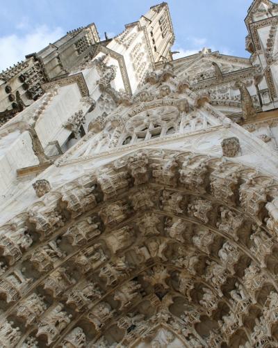1. A low-angle photograph of the ornate Gothic portal and facade of a large stone cathedral, featuring intricate sculptural details on the tympanum and archivolts under a blue sky.