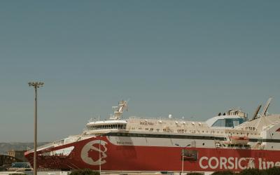 A large red and white ferry ship docked at a port, featuring the "CORSICA line" logo and name on its hull.