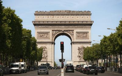 A view down a wide, tree-lined avenue with traffic and a large triumphal arch in the background.