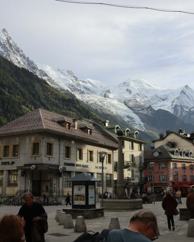 1. A town square in a mountainous alpine setting featuring multi-story buildings, a central fountain, pedestrians, and snow-capped peaks in the background.
