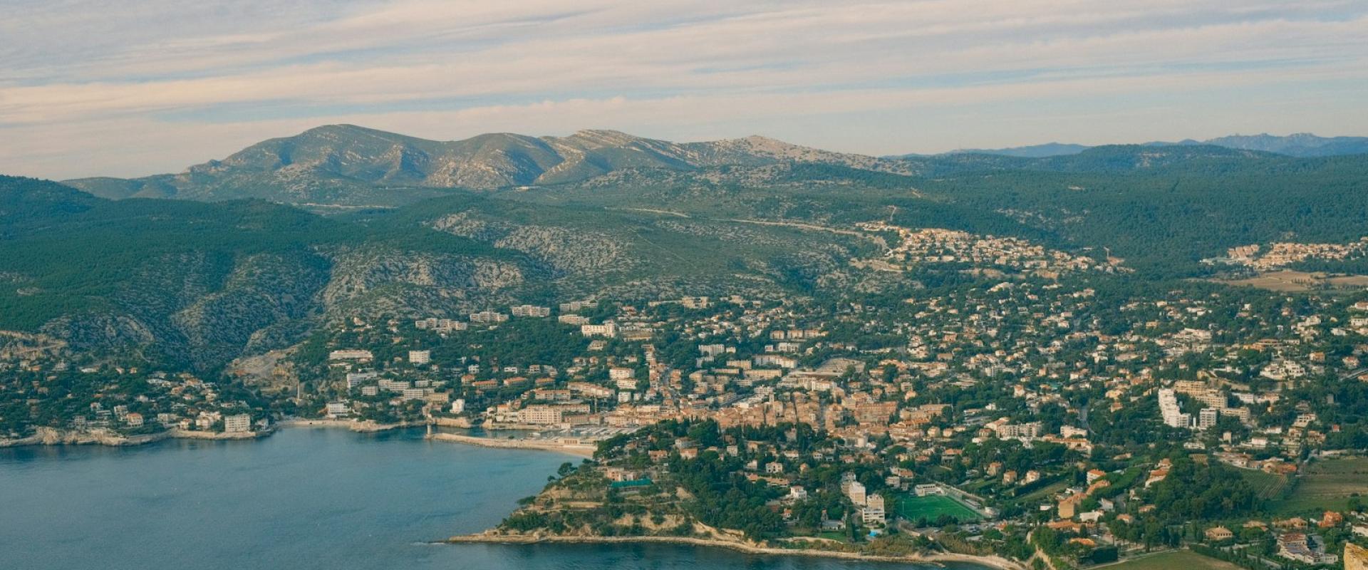 Aerial view of the coastal town of Cassis in the Calanques National Park, France, with the Mediterranean Sea and forested hills.