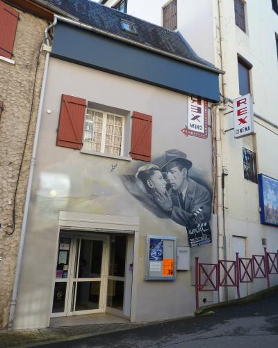 The image shows the exterior of a cinema building with a large mural of a man and woman, signage reading "CINEMA REX" and "STUDIO REX," and a vertical sign also reading "REX CINEMA."
