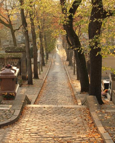 A cobbled, tree-lined avenue between the tombs of Père Lachaise cemetery in autumn