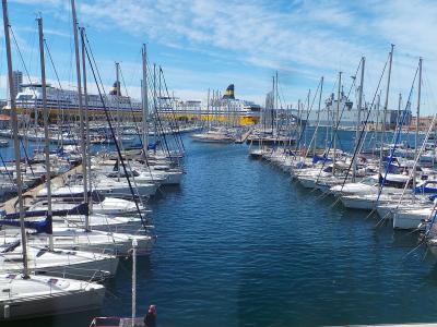 Toulon marina filled with sailboats, a yellow ferry, and the city skyline under a blue sky.