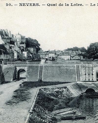 A vintage postcard showing a river scene with a stone bridge, buildings along the bank, and a French postage stamp, with printed text reading "20. — NEVERS. — Quai de la Loire. — Le Pont Mal-Placé."
