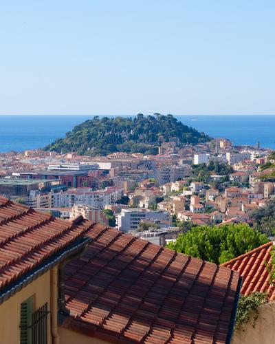 A high-angle view of the Nice coastline featuring a prominent green hill (Castle Hill) overlooking the Mediterranean Sea, with terracotta rooftops in the foreground and the filename indicating the photo was taken from Cimiez.