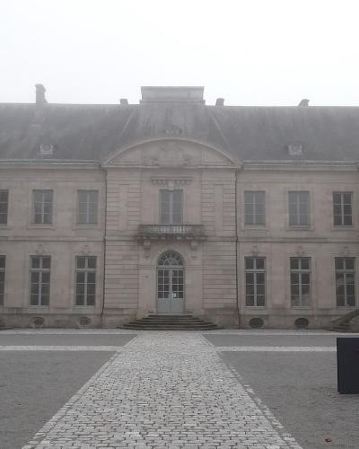 The Palais de l'Évêché in Limoges with a cobblestone path leading to the main entrance on a foggy day.