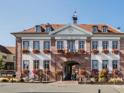 A large, two-story building with a central arched entrance, flower boxes, and a sign reading "HOTEL DE VILLE" under a pediment with a clock.