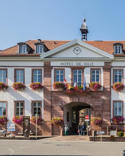 A large, two-story building with a central arched entrance, flower boxes, and a sign reading "HOTEL DE VILLE" under a pediment with a clock.