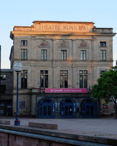 The image shows a large, classical-style stone building with "THEATRE MUNICIPAL" inscribed on its facade and a pink banner reading "le Granit scène nationale" above the entrance.