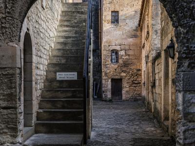 A narrow cobblestone alleyway in a historic stone village, viewed through a rough-hewn stone archway, with an external stone staircase and a sign reading "Privé - Accès interdit / Private - No access".