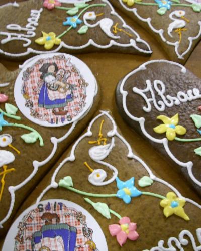 A close-up view of several decorated gingerbread cookies (pain d'épices) featuring white icing designs, colorful sugar flowers, and circular edible paper inserts depicting figures in traditional Alsatian dress with text like "Alsace" and "SAIT".
