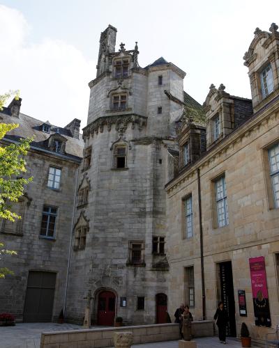 A courtyard view of the historic Palace of the Bishops of Cornouaille in Quimper, France, featuring a prominent stone tower with Gothic and Renaissance architectural details, adjacent wings, and signage for the Musée Départemental Breton.