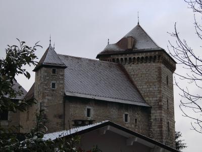 A stone medieval castle with two prominent towers featuring steep, snow-dusted roofs and crenellated battlements, viewed from a low angle with foliage in the foreground.