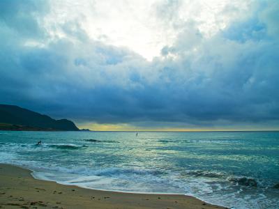 Dramatic cloudy sky over turquoise ocean waves breaking on a sandy beach with a distant headland.