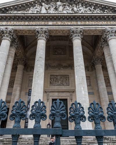 A close-up of the pediment and entablature of a neoclassical building, featuring sculptural reliefs and the French inscription "AUX HOMMES LA PATRIE RECONNAISSANTE" (To the men the grateful fatherland) in gold lettering above Corinthian columns.
