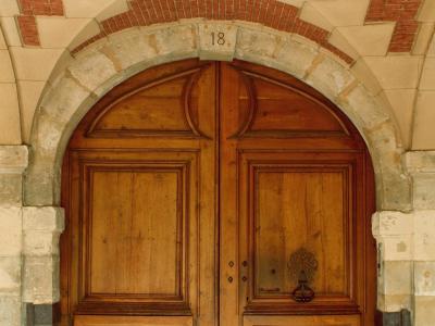 A close-up of a large, arched green wooden door set within a stone archway, with a blue house number plaque reading "24" on the left jamb.