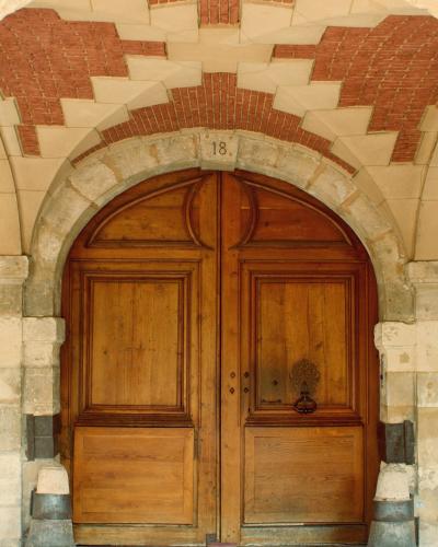 A close-up of a large, arched green wooden door set within a stone archway, with a blue house number plaque reading "24" on the left jamb.