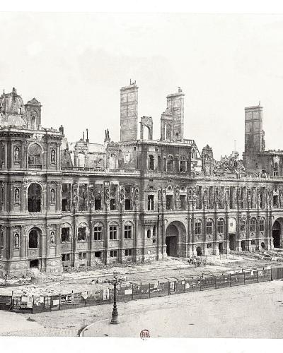 A black-and-white historical photograph showing a large, ornate, multi-story building with extensive fire damage, collapsed roofs, exposed chimneys, and debris-strewn grounds, consistent with the aftermath of the Paris Commune in 1871; no visible