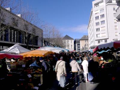 A crowded outdoor street market with colorful vendor stalls and awnings, set between modern and traditional buildings under a clear blue sky.