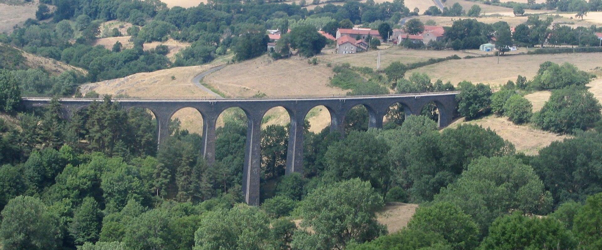 1. A long, multi-arched stone railway viaduct spanning a lush green valley with scattered trees and fields, under a hazy sky; no visible signage or text.