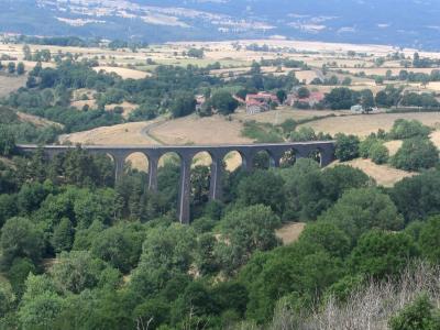 1. A long, multi-arched stone railway viaduct spanning a lush green valley with scattered trees and fields, under a hazy sky; no visible signage or text.