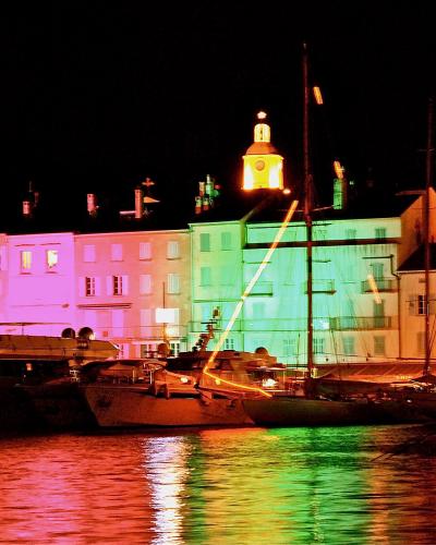 A night view of a harbor with colorful buildings and boats, featuring a prominent illuminated church tower in the background.