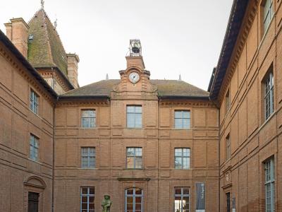 Brick courtyard of Musée Ingres-Bourdelle featuring a statue, clock tower, and banner.