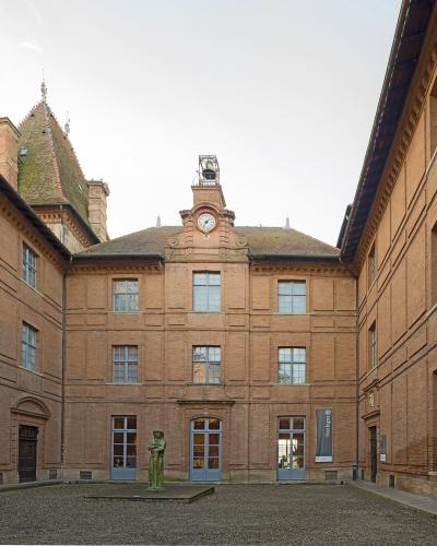 Brick courtyard of Musée Ingres-Bourdelle featuring a statue, clock tower, and banner.