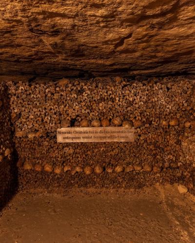 1. A large, cylindrical ossuary structure constructed from neatly stacked human femurs and skulls, situated within a rough-hewn limestone tunnel with a stone cross visible on the left wall.