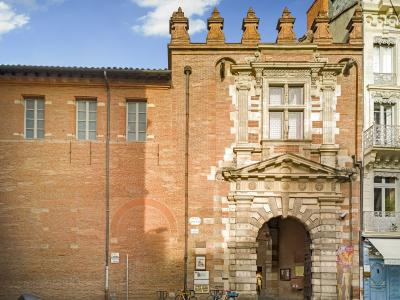 The image shows the main entrance facade of a historic brick building with a prominent stone archway, decorative Renaissance-style stonework around the doorway and upper window, and a crenellated parapet; a street sign reading "PLACE D'ASSEZAT" is