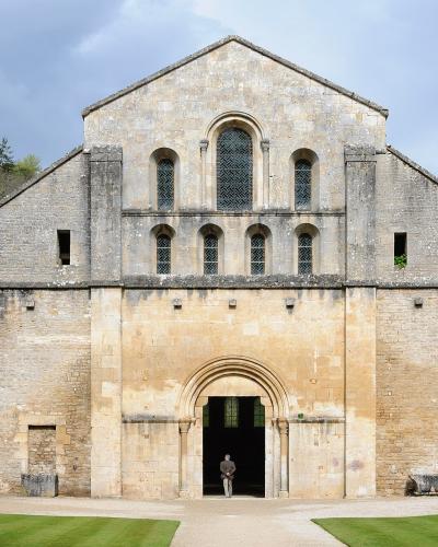 A person stands in the arched doorway of the Abbey Church of Fontenay, a historic Cistercian building in Marmagne, France.