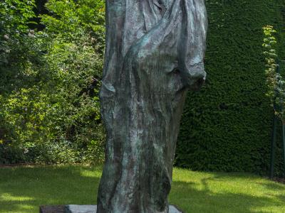 A bronze sculpture of a nude female figure leaning against a rough-hewn rock, with arms crossed over her chest and head bowed, set against a plain white background.