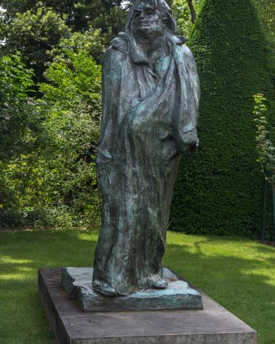 A bronze sculpture of a nude female figure leaning against a rough-hewn rock, with arms crossed over her chest and head bowed, set against a plain white background.