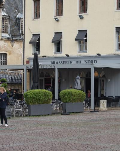 The image shows an outdoor plaza with a brasserie named "BRASSERIE DU NORD" on the ground floor of a building, with people standing on a cobblestone surface and a yellow sign in the bottom left corner reading "VILLE DE CLUNY".