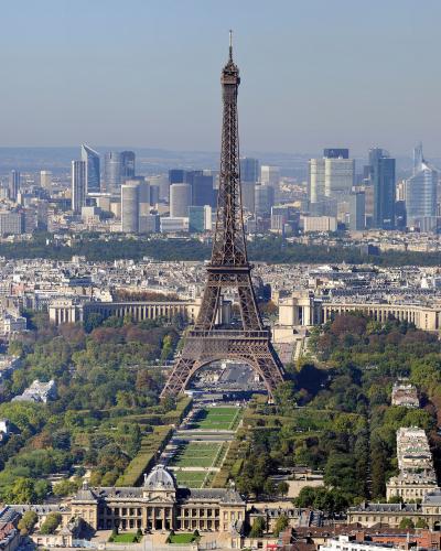 The Eiffel Tower rises from the Champ de Mars gardens with the La Défense skyline in the background.